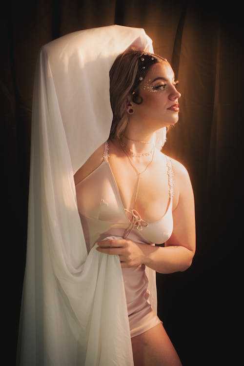 A woman in lingerie is posing in front of a white curtain