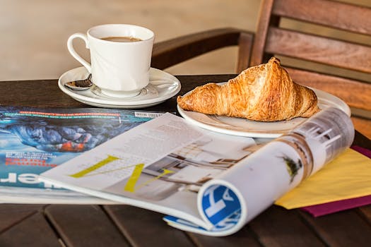 Enjoy a peaceful morning with coffee, croissant, and reading material on a wooden table.
