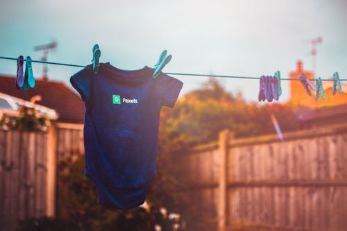Free Blue baby onesie hanging on clothesline with clothespins in sunny backyard setting. Stock Photo