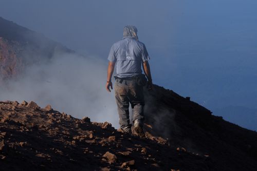 Free A solitary hiker in rugged terrain near volcanic smoke, showcasing adventure and resilience. Stock Photo