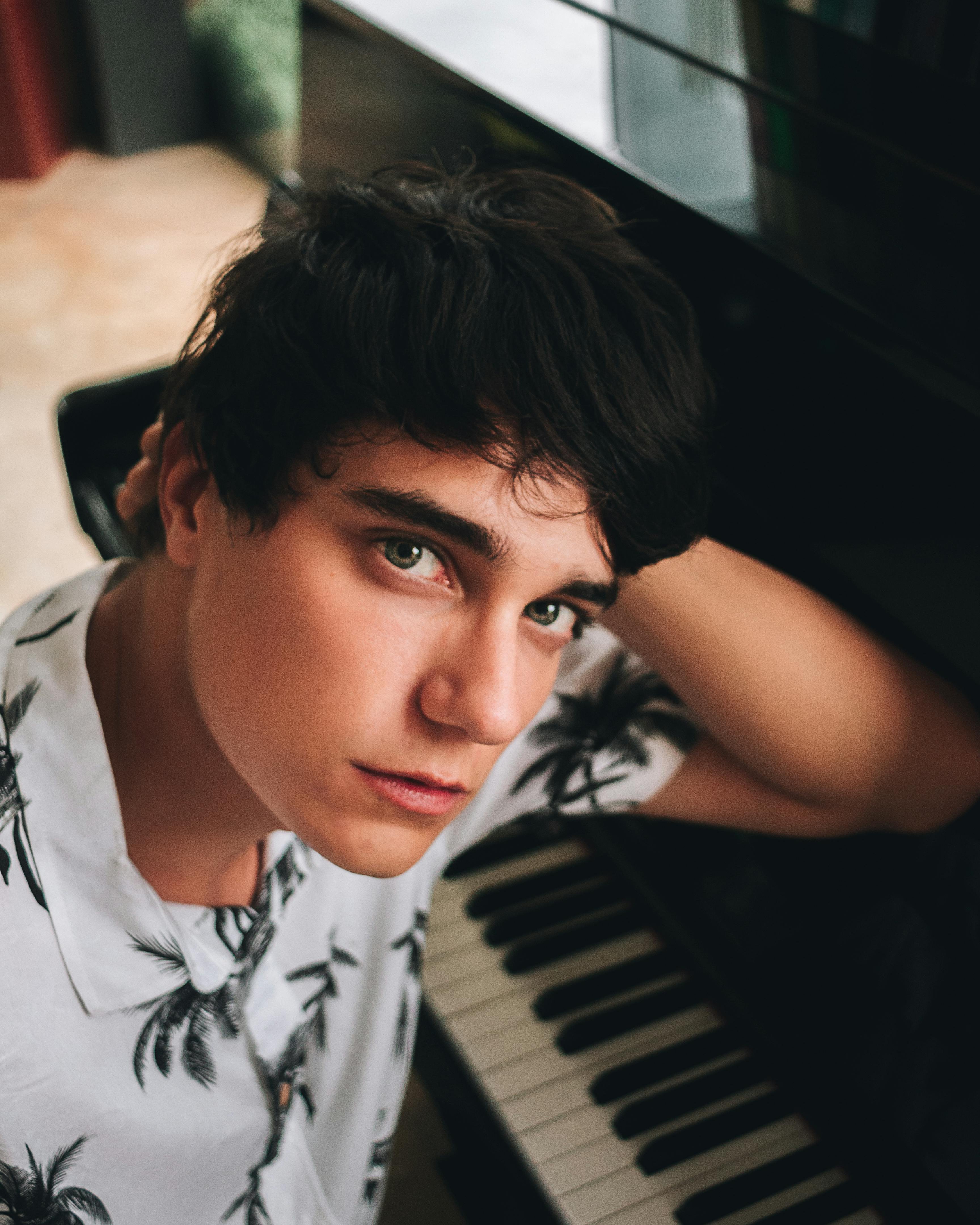 室内，一名黑发年轻人若有所思地在三角钢琴前摆姿势