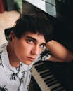 室内，一名黑发年轻人若有所思地在三角钢琴前摆姿势