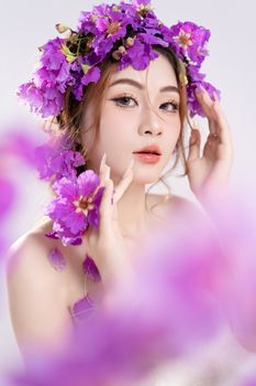 A captivating studio portrait of a woman adorned with a vibrant purple floral wreath against a white background.