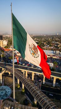 A stunning aerial view showcasing the Mexican flag over Mexico City's urban landscape and roads.