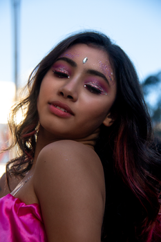 Portrait of a young woman with glitter makeup and pink attire, exuding confidence outdoors.