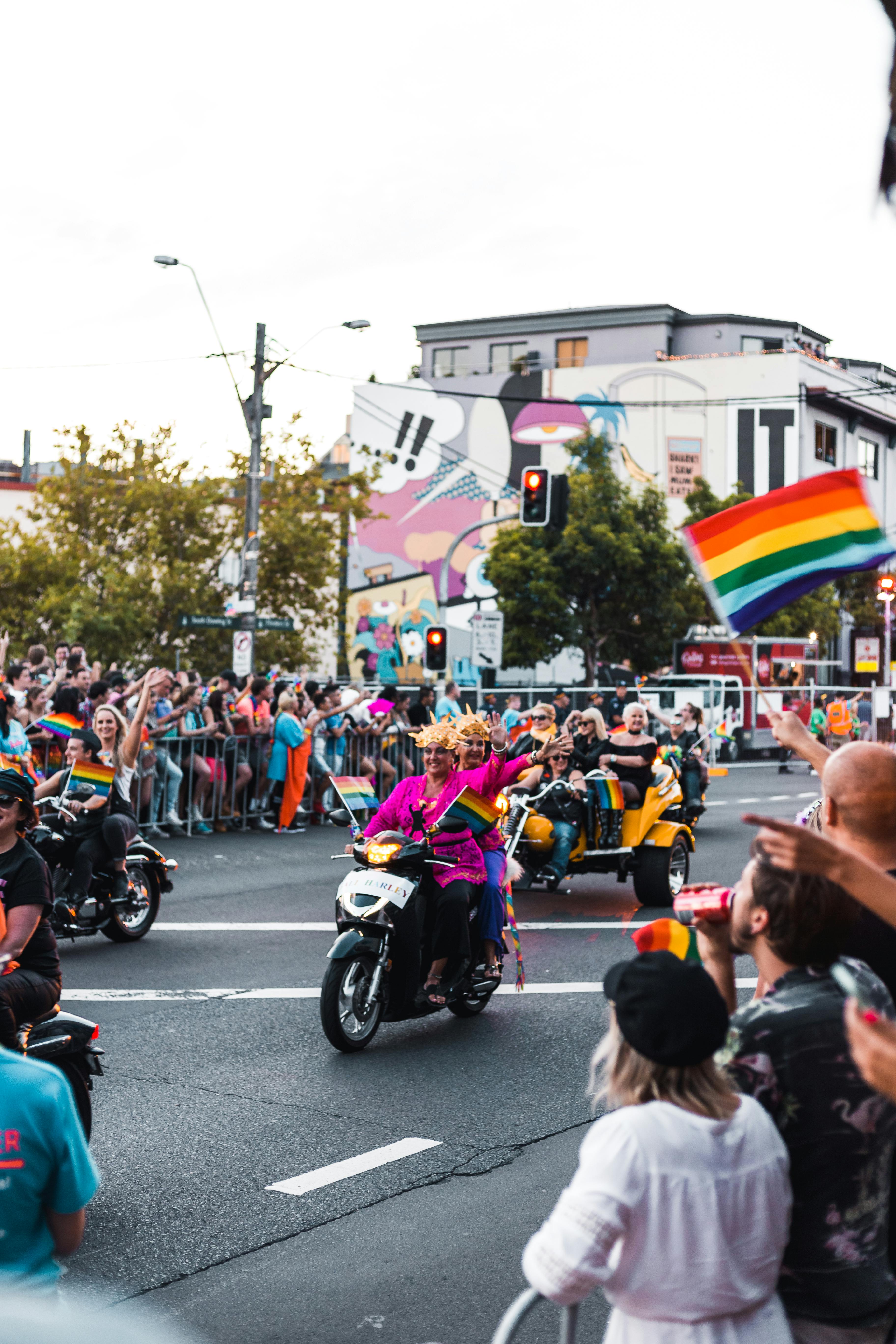 Lively LGBTQ parade in the city featuring motorcycles, rainbow flags, and a cheering crowd.