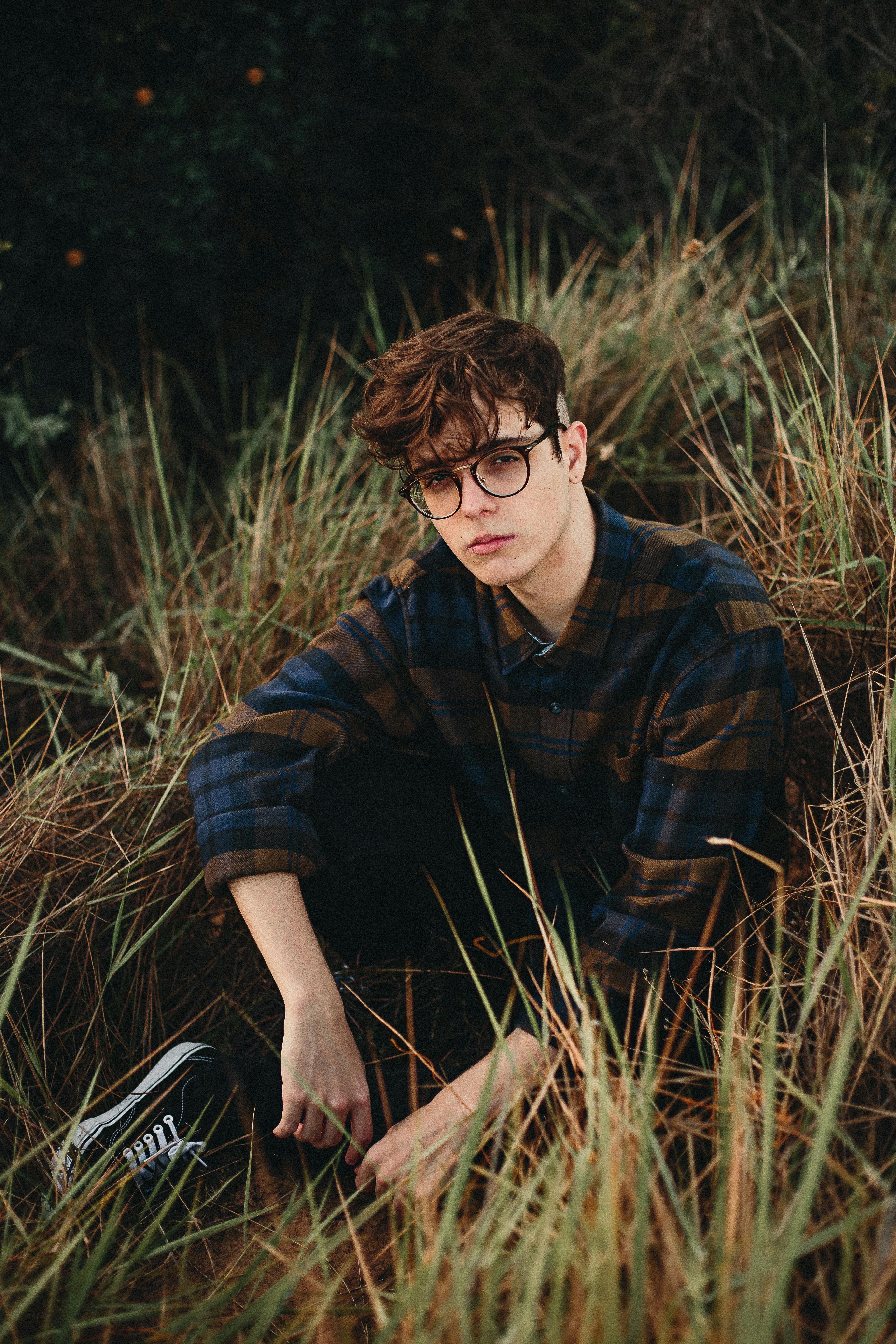 一个戴着眼镜、穿着休闲服的年轻人，在高高的草丛中摆着姿势