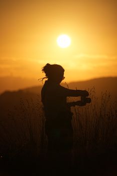 A woman silhouetted against a vibrant sunset, standing in a field of tall grass, conveying tranquility and beauty.