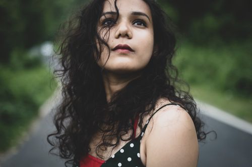 Free A contemplative woman with curly hair gazes upwards on a road surrounded by greenery. Stock Photo