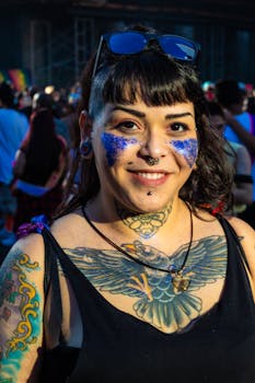 A smiling woman with tattoos and glitter poses at a lively music festival in São Paulo, Brazil.