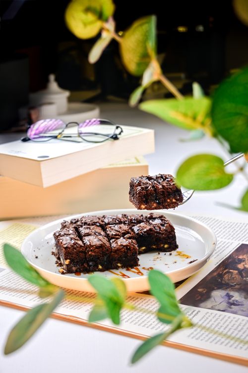 Free Freshly baked chocolate brownies on plate with books and eyeglasses nearby, creating a cozy atmosphere. Stock Photo