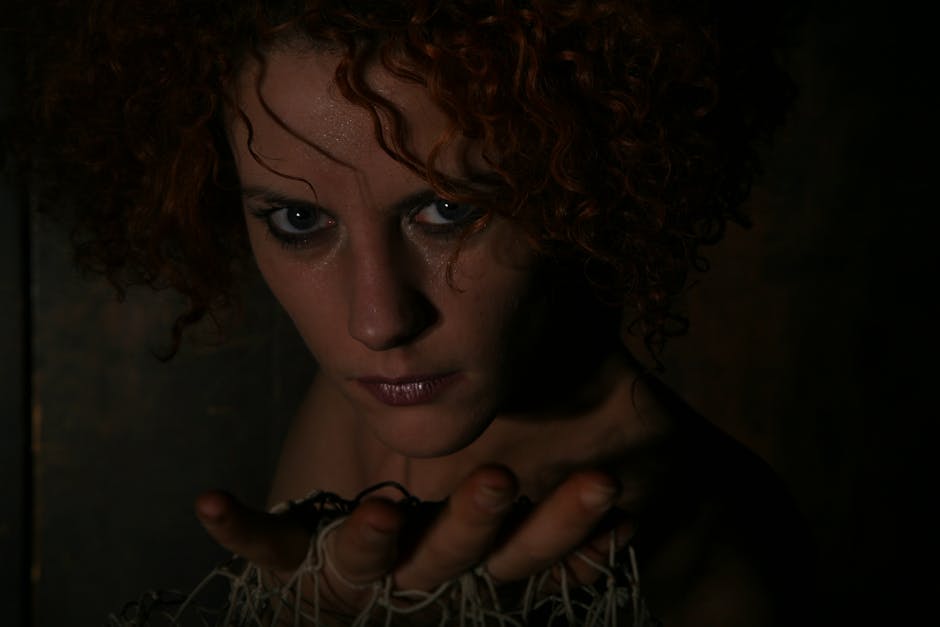 Intense portrait of a woman with curly red hair in dim lighting, conveying a dramatic mood.