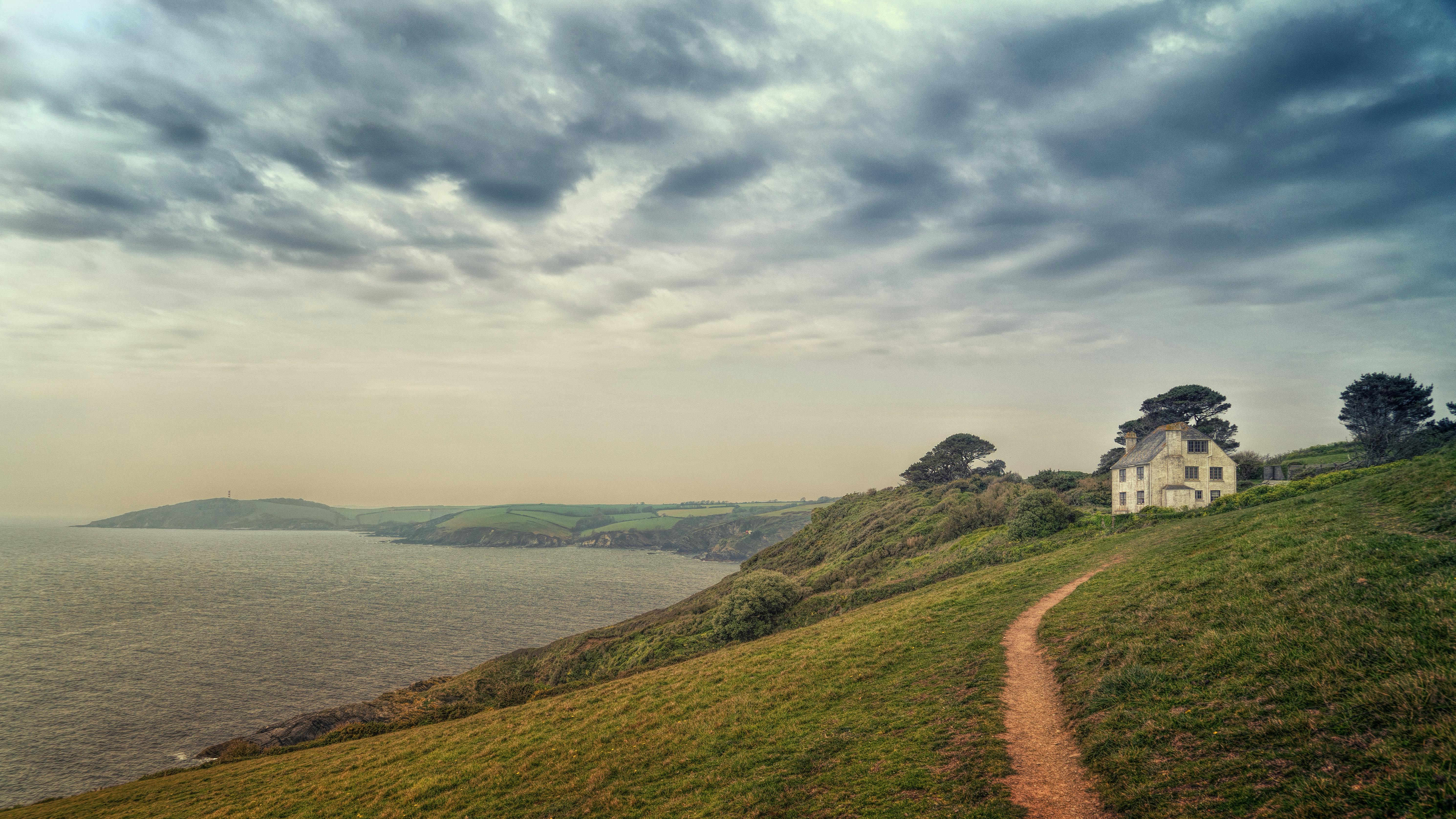 在田园诗般的海岸边，一条小路通向古色古香的小屋，小屋上方是戏剧性的天空