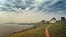 在田园诗般的海岸边，一条小路通向古色古香的小屋，小屋上方是戏剧性的天空