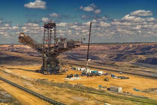 Aerial view of heavy machinery operating in a vast open-pit mine under a cloudy sky.
