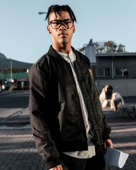 一位戴着眼镜的年轻人在南非的城市背景下，自信地以休闲时尚的姿态摆出姿势