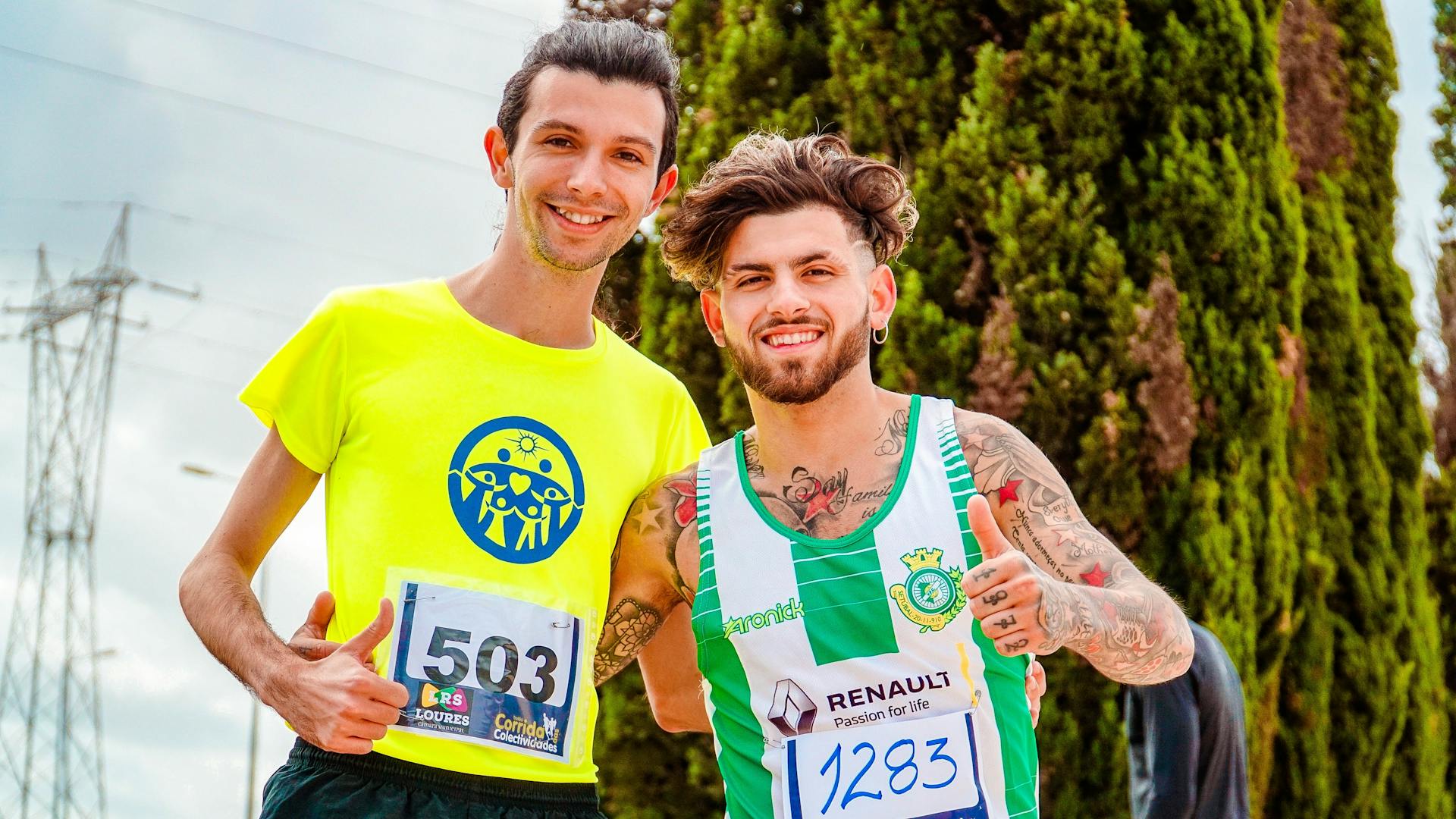 Two men posing happily with marathon bibs, outdoors on a sunny day.