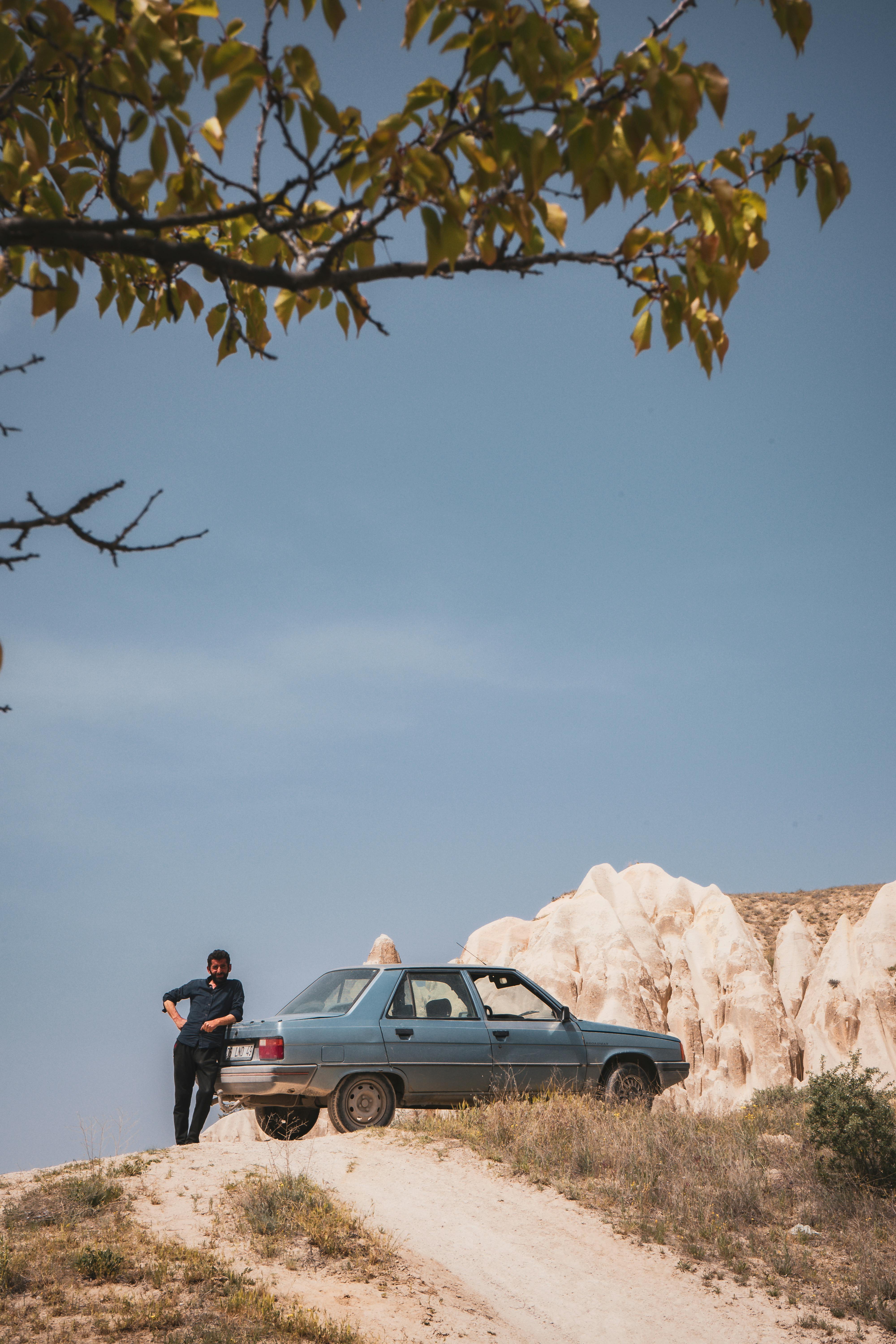 A person standing by a car on a rocky landscape in Göreme, Turkey, under a clear blue sky.