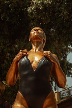 A striking golden sculpture of a woman in a swimsuit, captured in sunlight.