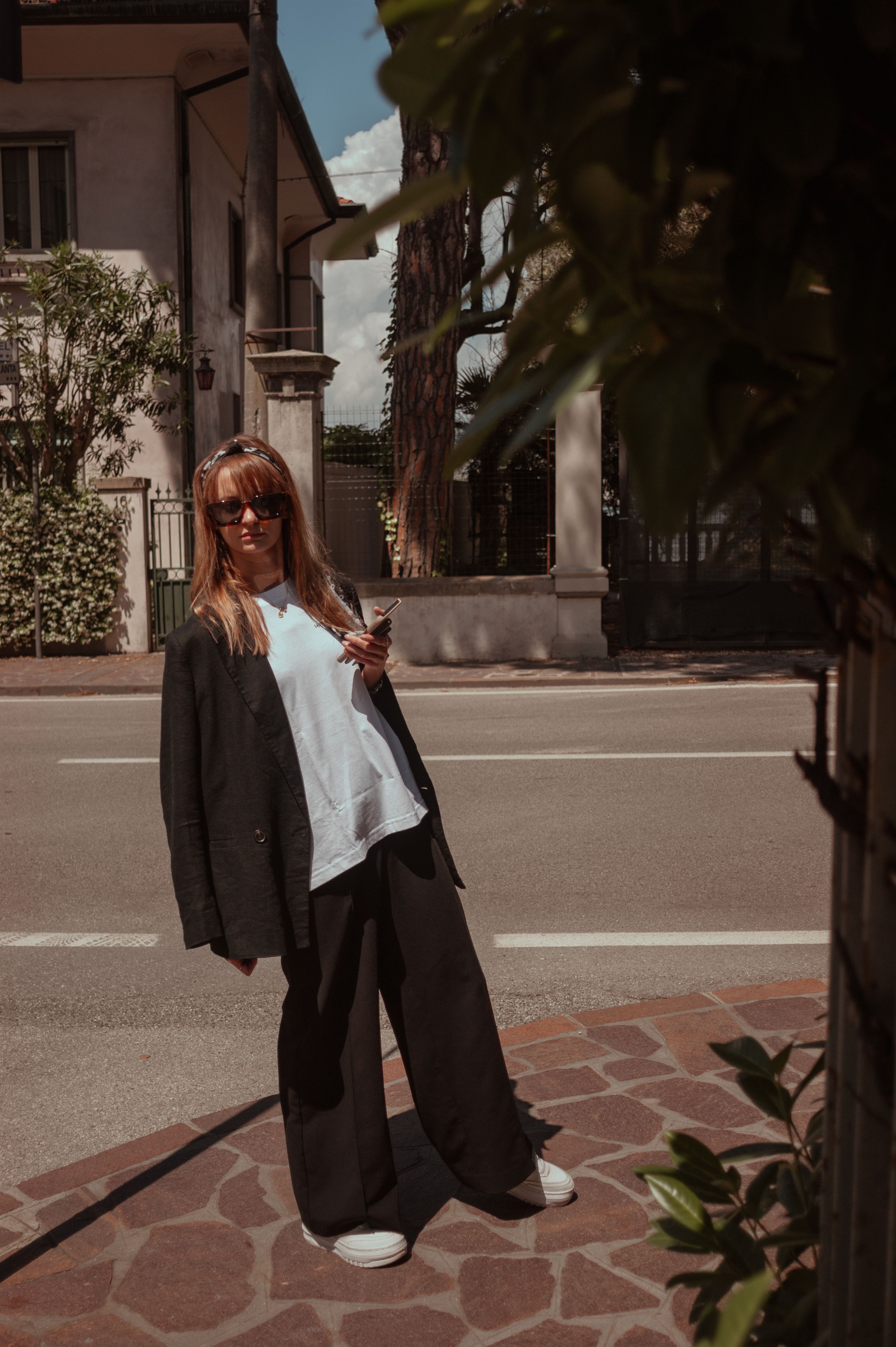 Woman in Black Jacket Standing on Sunlit Street · Free Stock Photo