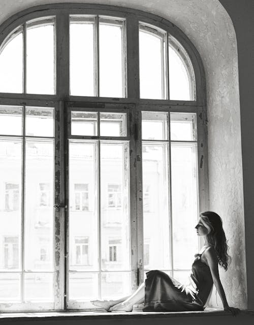 A woman sitting on a window sill in black and white