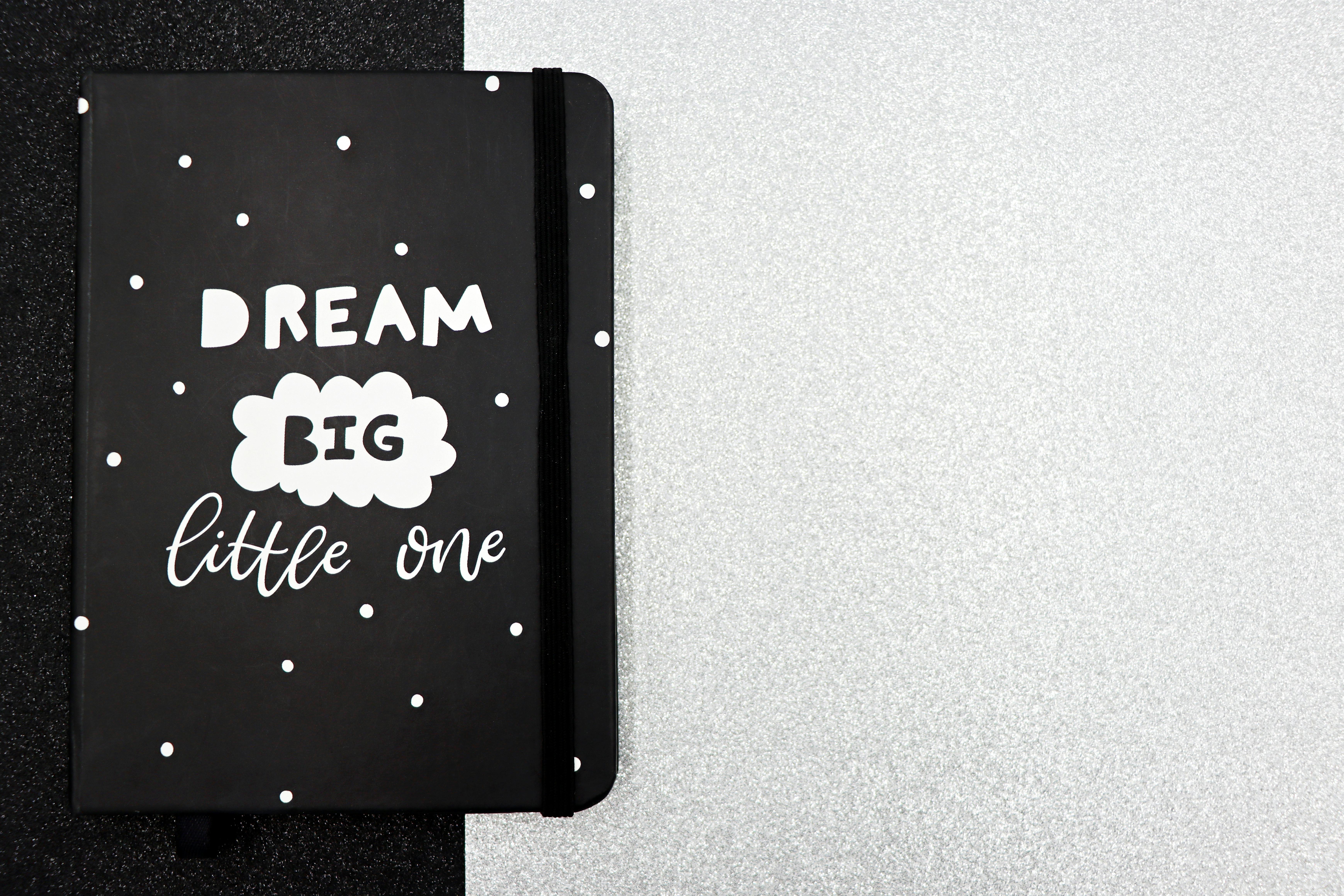 Black notebook with 'Dream Big Little One' quote on textured background, perfect for inspiration.