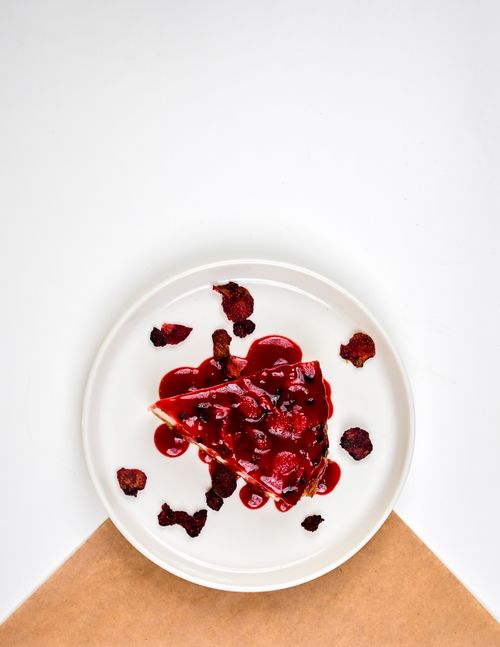 Free Top-down view of a cheesecake slice with berry glaze and dried fruit on a white plate. Stock Photo