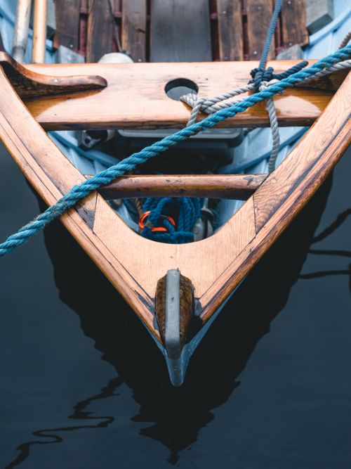 Free Detailed view of a wooden boat's bow with ropes, captured on calm water. Stock Photo