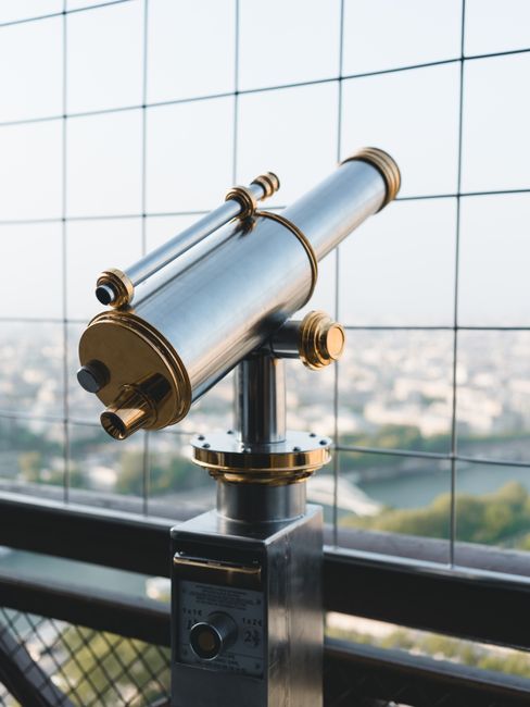Elegant brass telescope overlooking Paris from the Eiffel Tower platform.