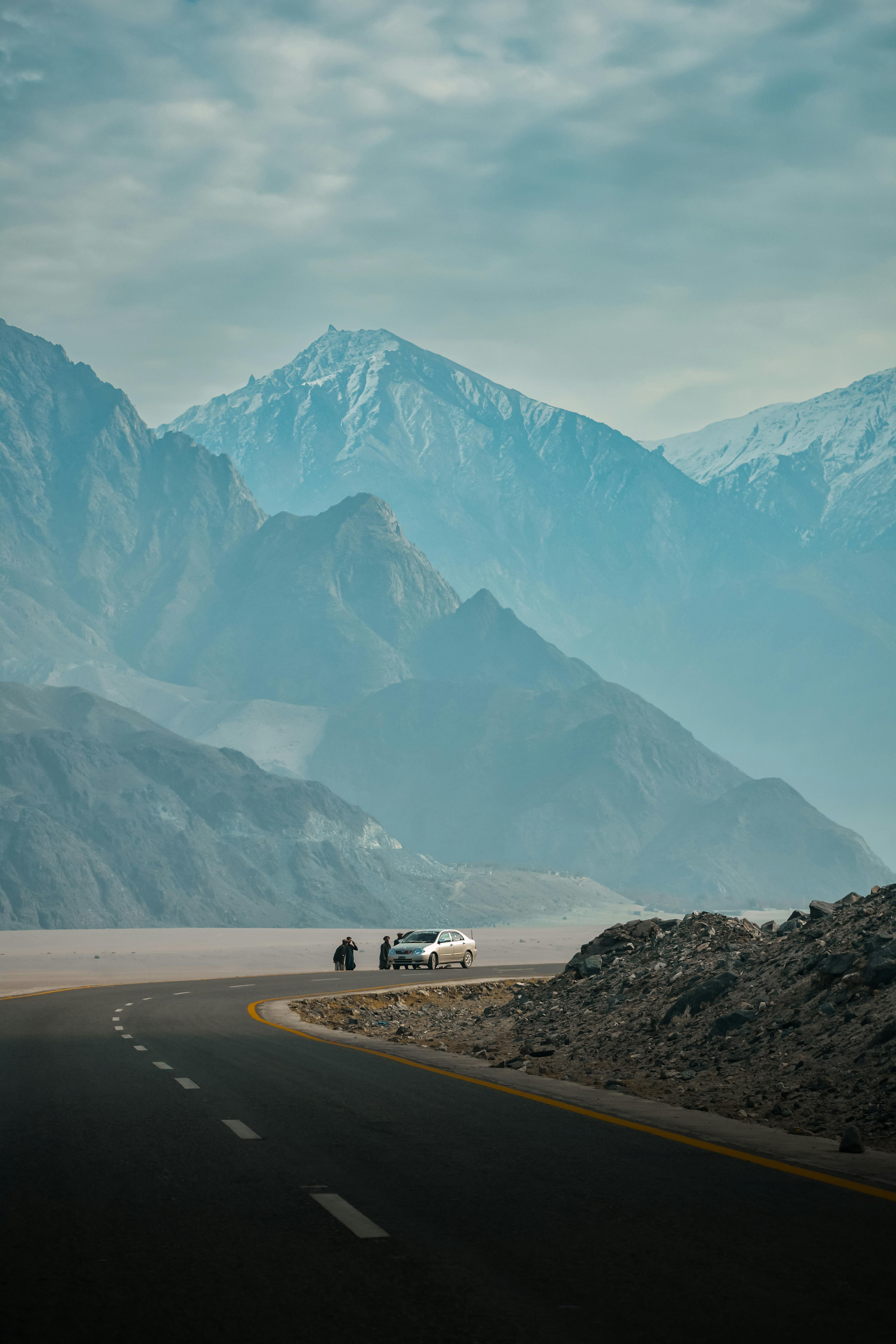 A car travels a winding road amid majestic mountains, capturing nature's grandeur.