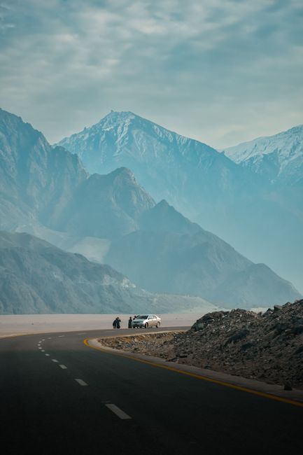 A car travels a winding road amid majestic mountains, capturing nature's grandeur.