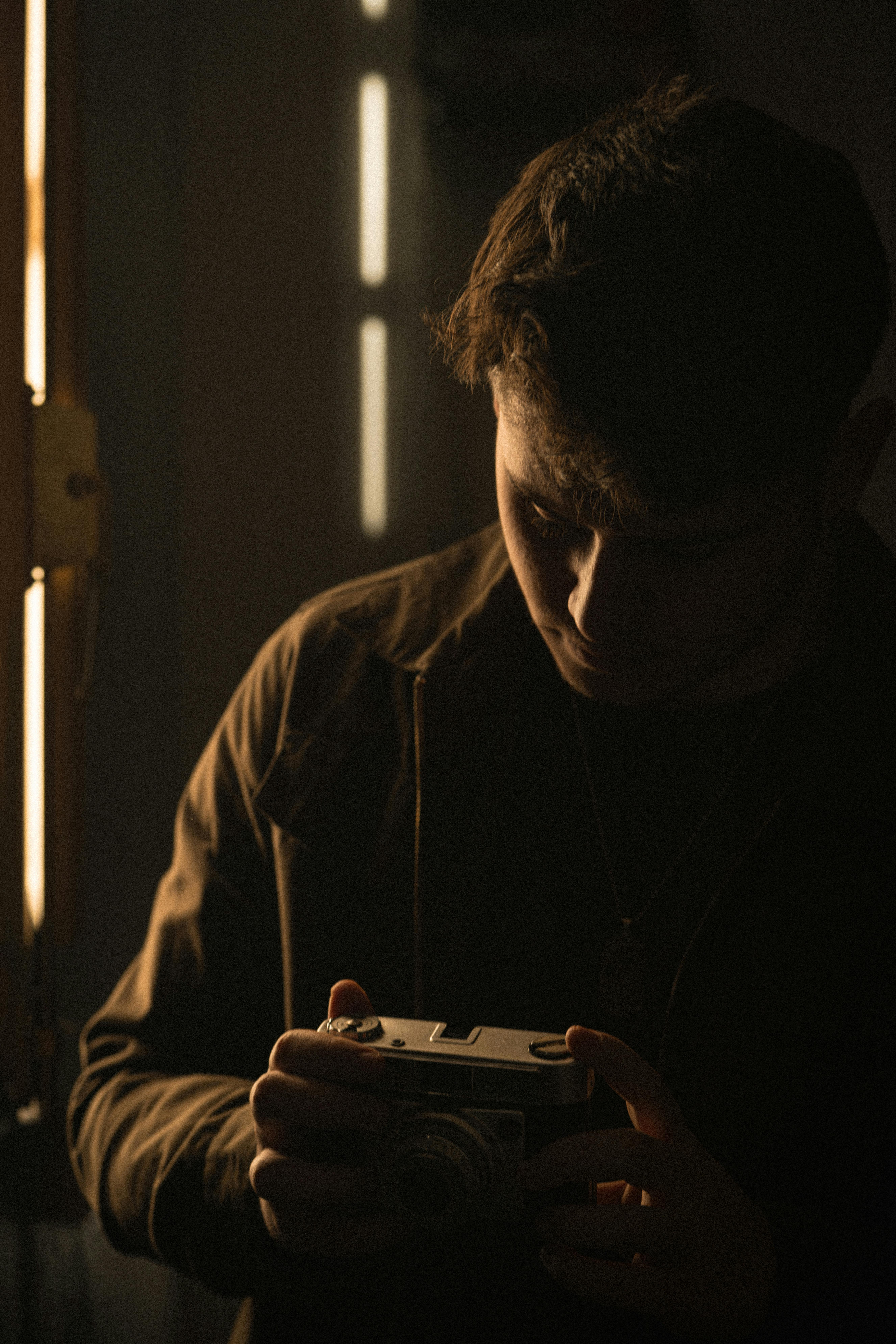 A man in low light holding a camera, reflecting dark and introspective mood.