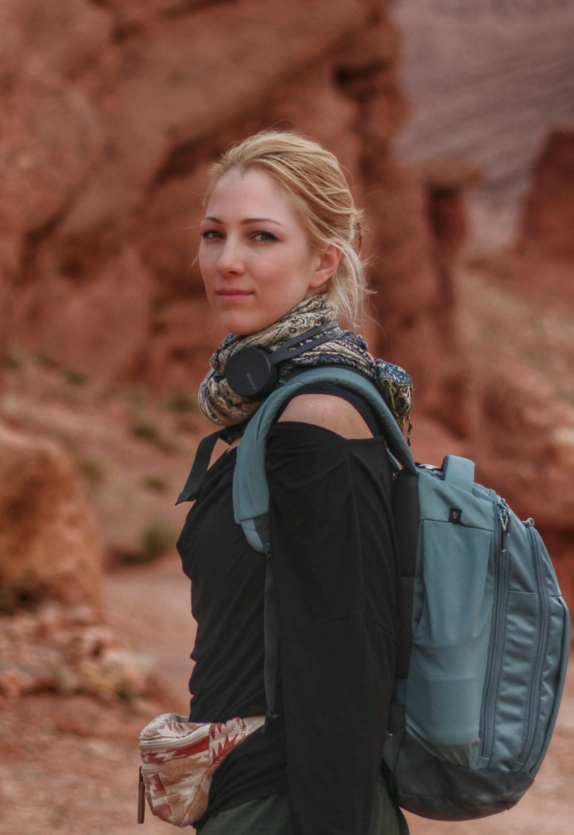 Fashionable woman with backpack and headphones hiking in a desert canyon. Outdoor adventure.
