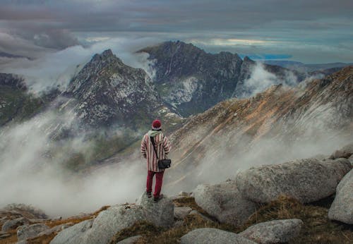 A person standing on top of a mountain looking at the clouds