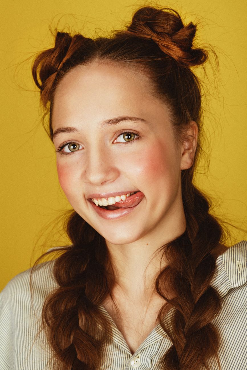 Cheerful young woman with braided hair smiling against a yellow background.