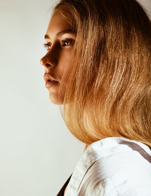 Elegant side profile portrait of a young woman with blonde hair in natural lighting.