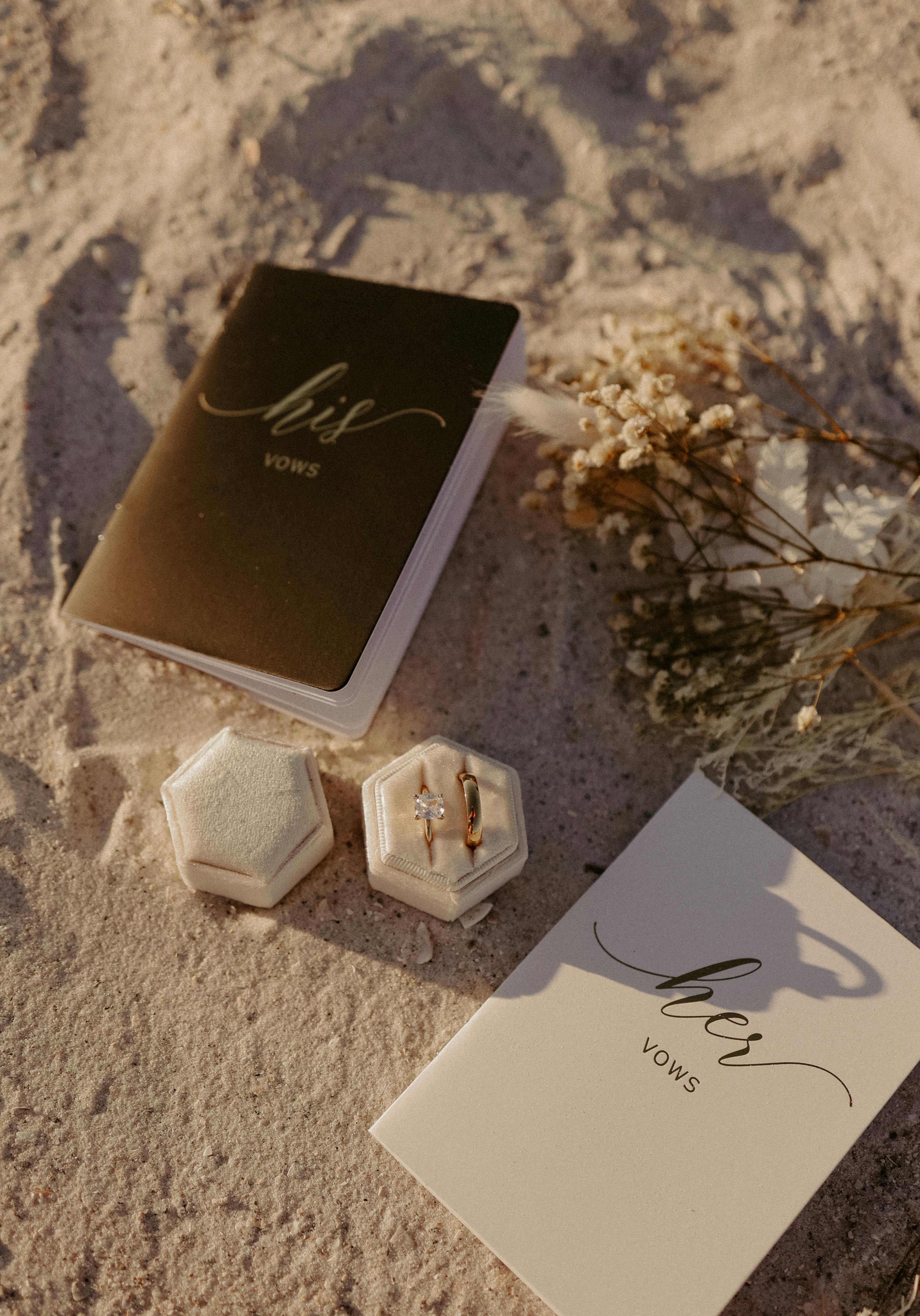 vows notebooks and wedding rings on sandy beach