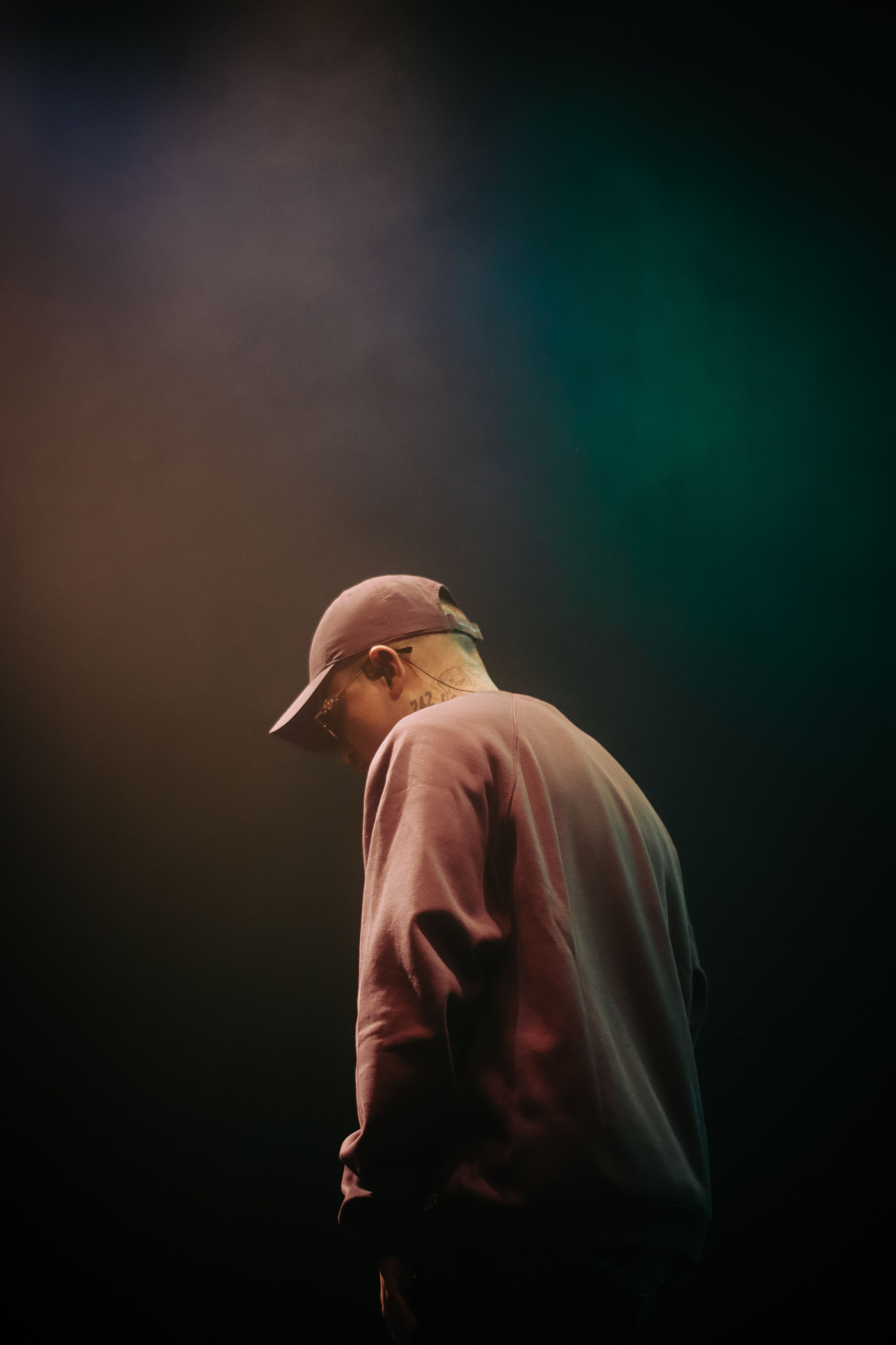 Side view of a man in a cap under spotlight, evoking a moody atmosphere in a studio setting.