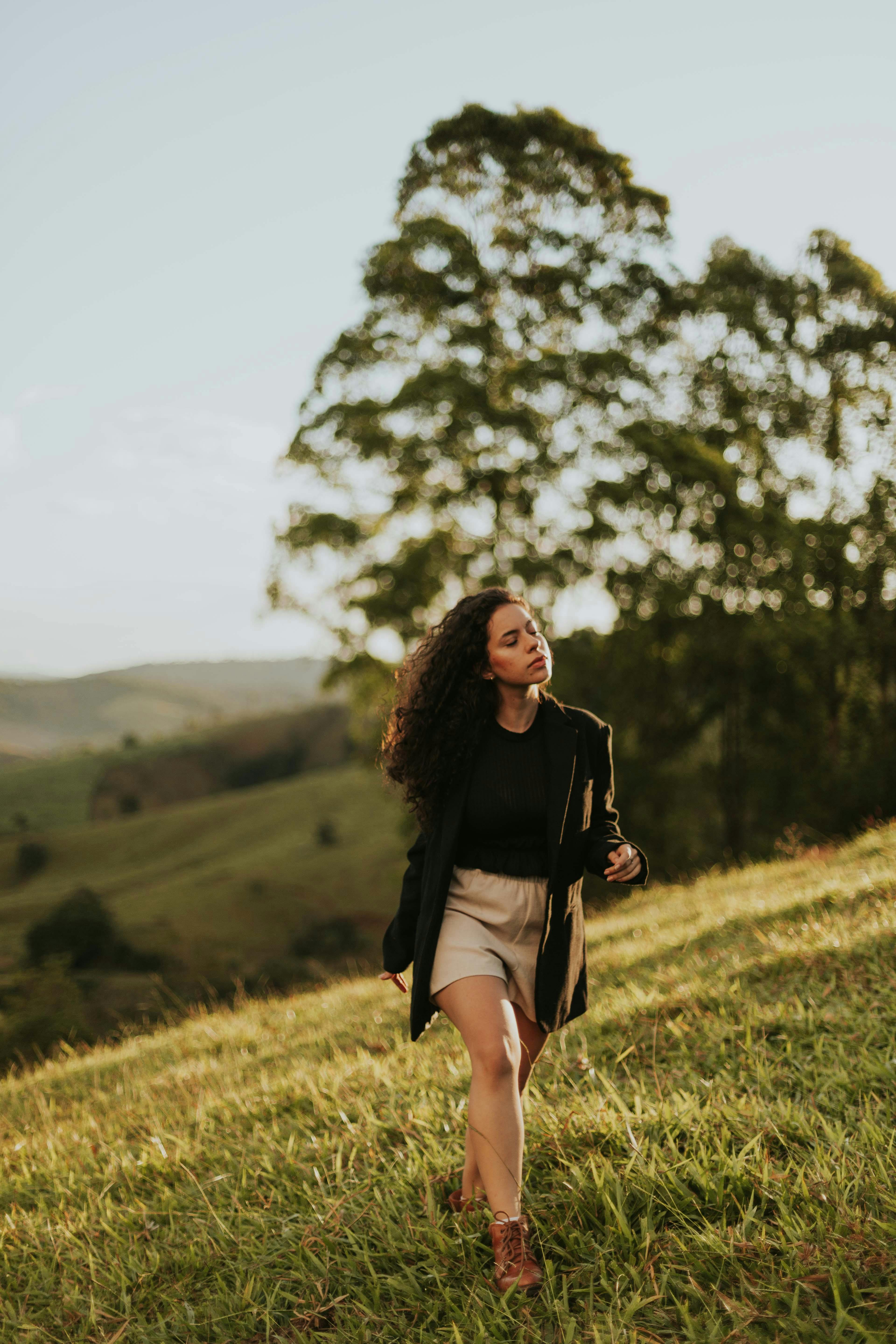 Fashionable woman strolling through a lush meadow under warm sunlight. Captured on Canon EOS 5D Mark III.
