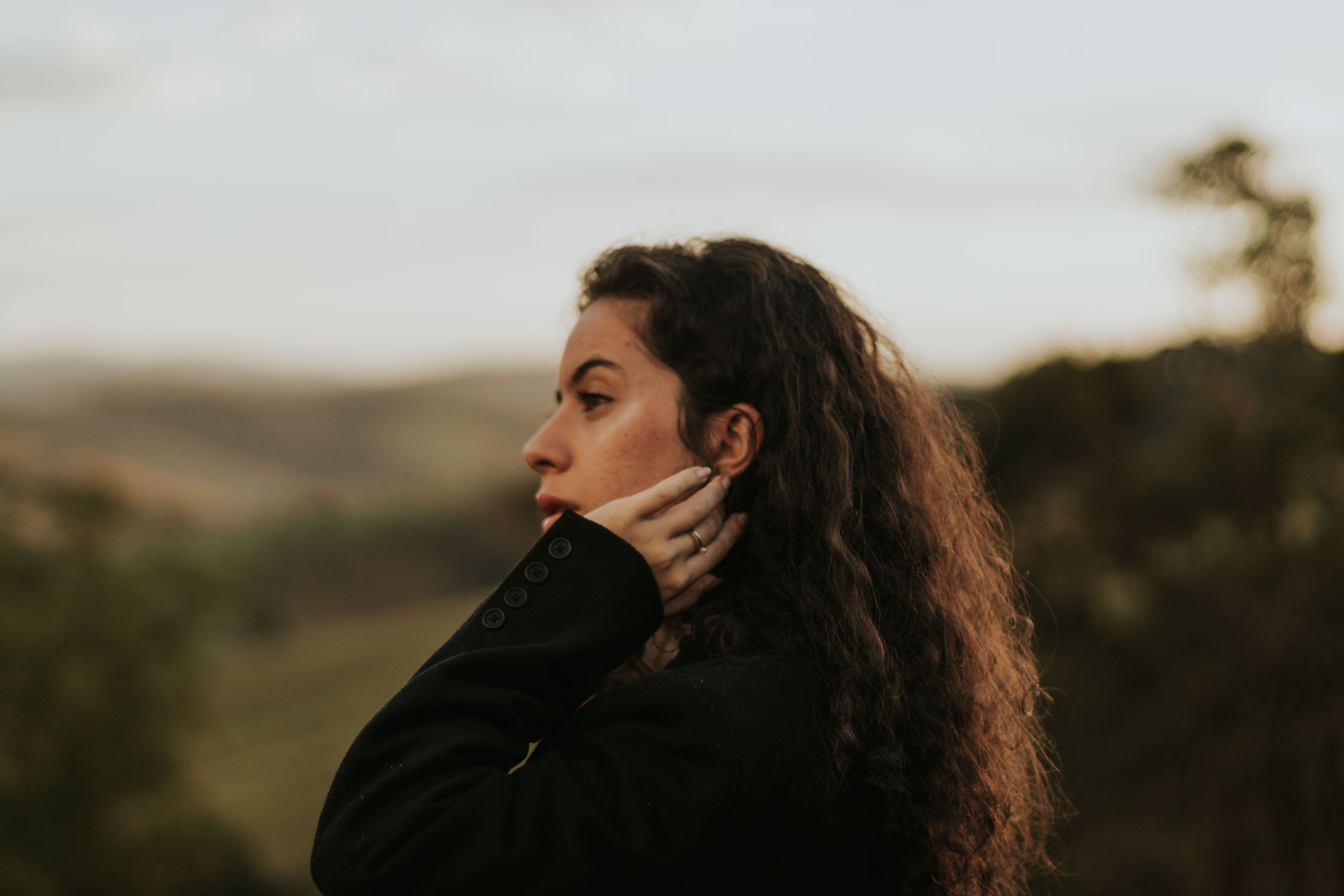 Mulher sentada ao ar livre, olhar contemplativo, luz natural suave ao entardecer