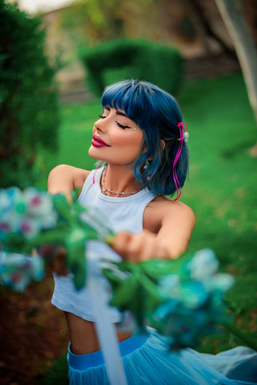 Free Fashionable woman with blue hair posing in a garden, eyes closed, wearing a tank top. Stock Photo