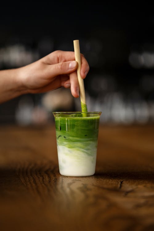 A person holding a wooden stick in a glass of green tea