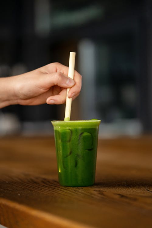 A person holding a straw in a green drink