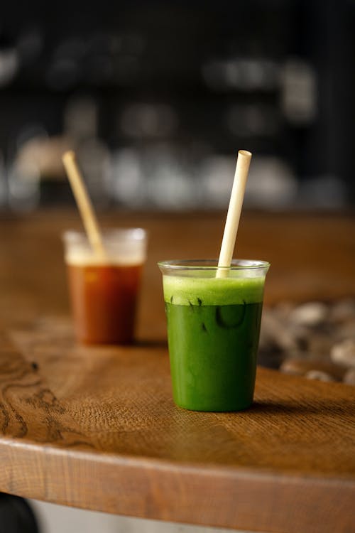 Two cups of green juice with straws on a wooden table