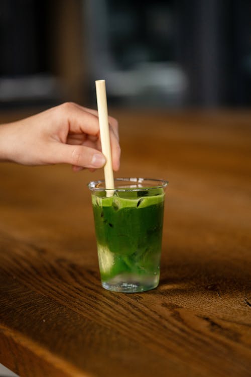 A person holding a straw in a green drink
