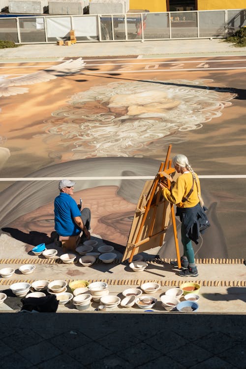 Two people painting on the street with a large canvas