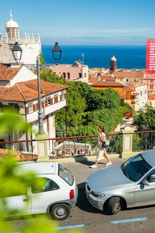 A woman walking down a street with cars parked in front of her