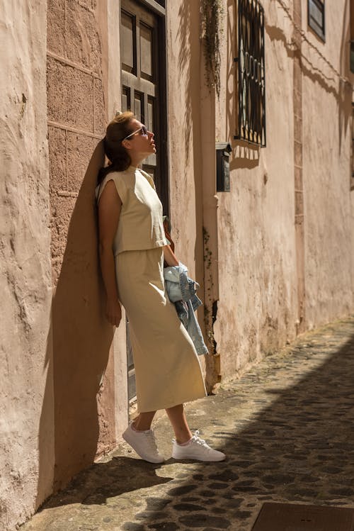 A woman in a yellow dress and white sneakers standing on a narrow street