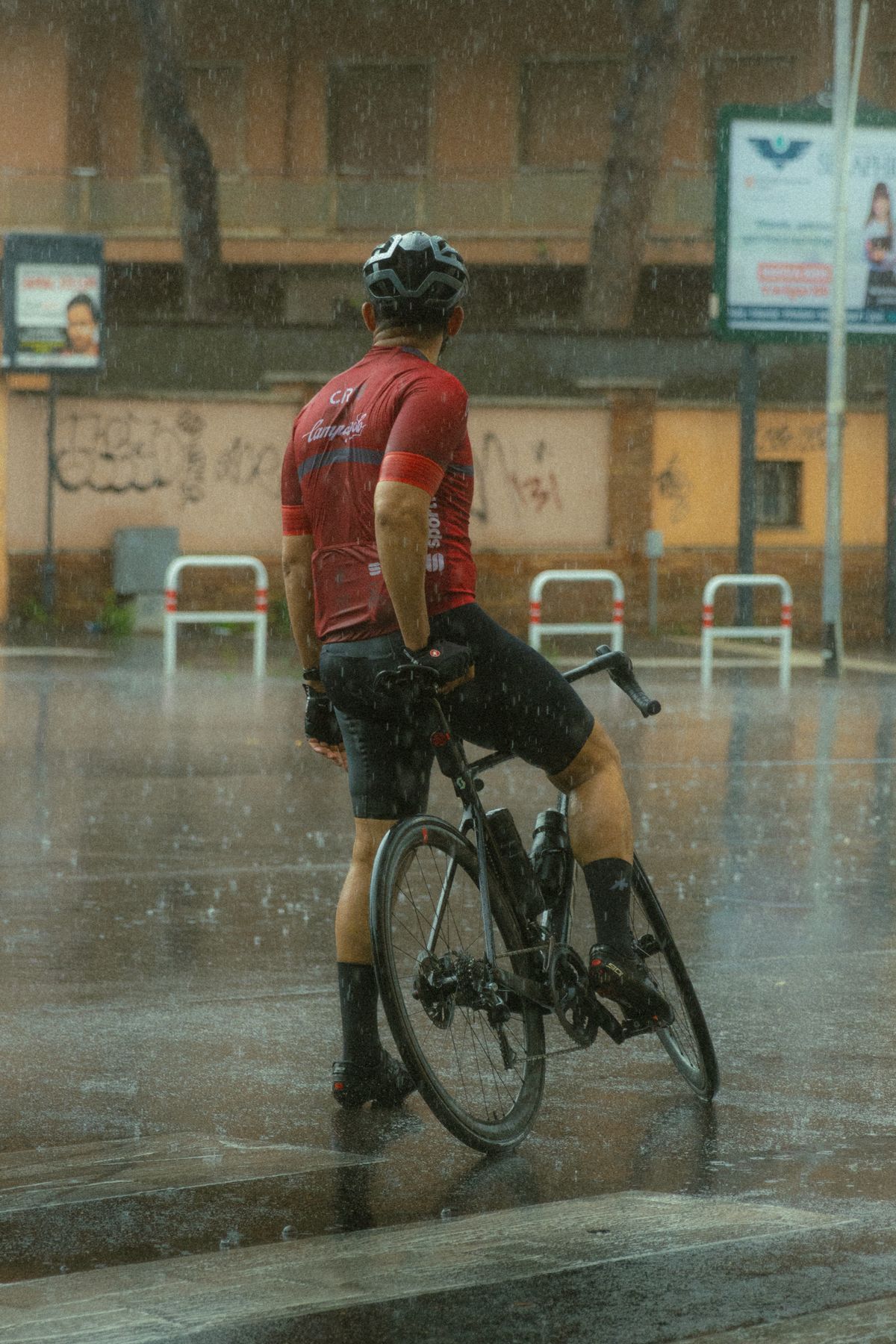 Helmeted cyclist waiting at a rainy city intersection with practical weather gear