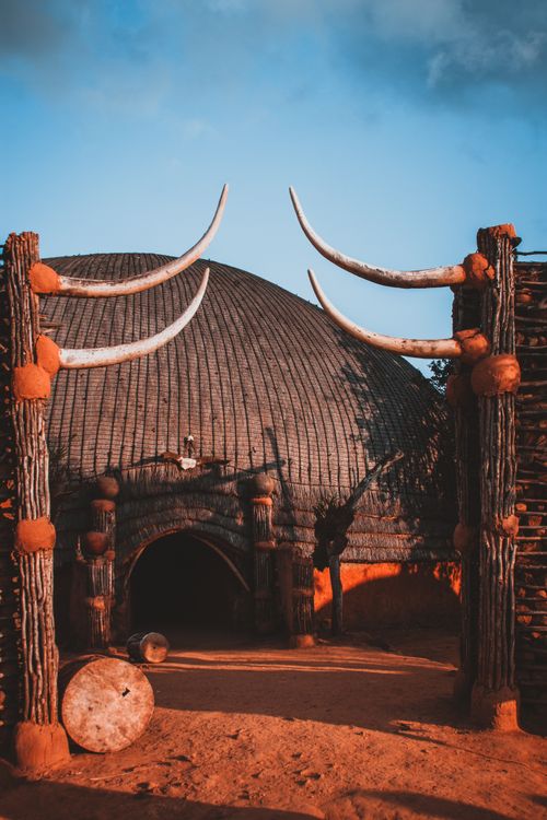 Free A stunning traditional African hut with a rustic wooden archway, bathed in warm sunset light. Stock Photo